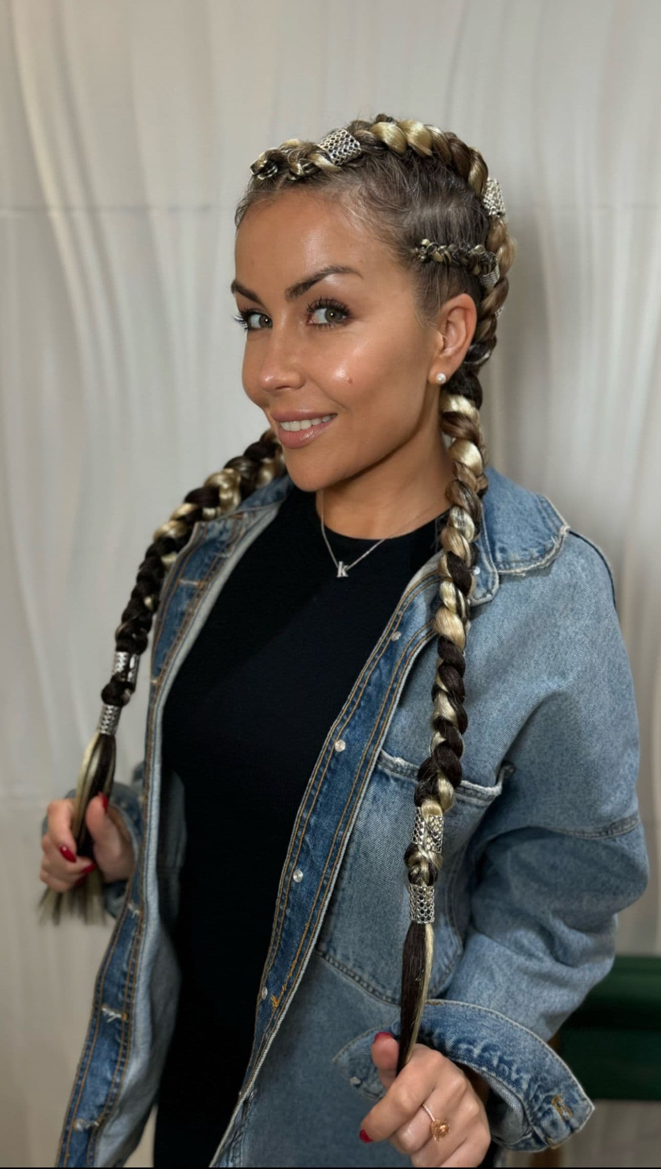 A smiling woman with blonde and brown Dutch braids, adorned with silver accents.