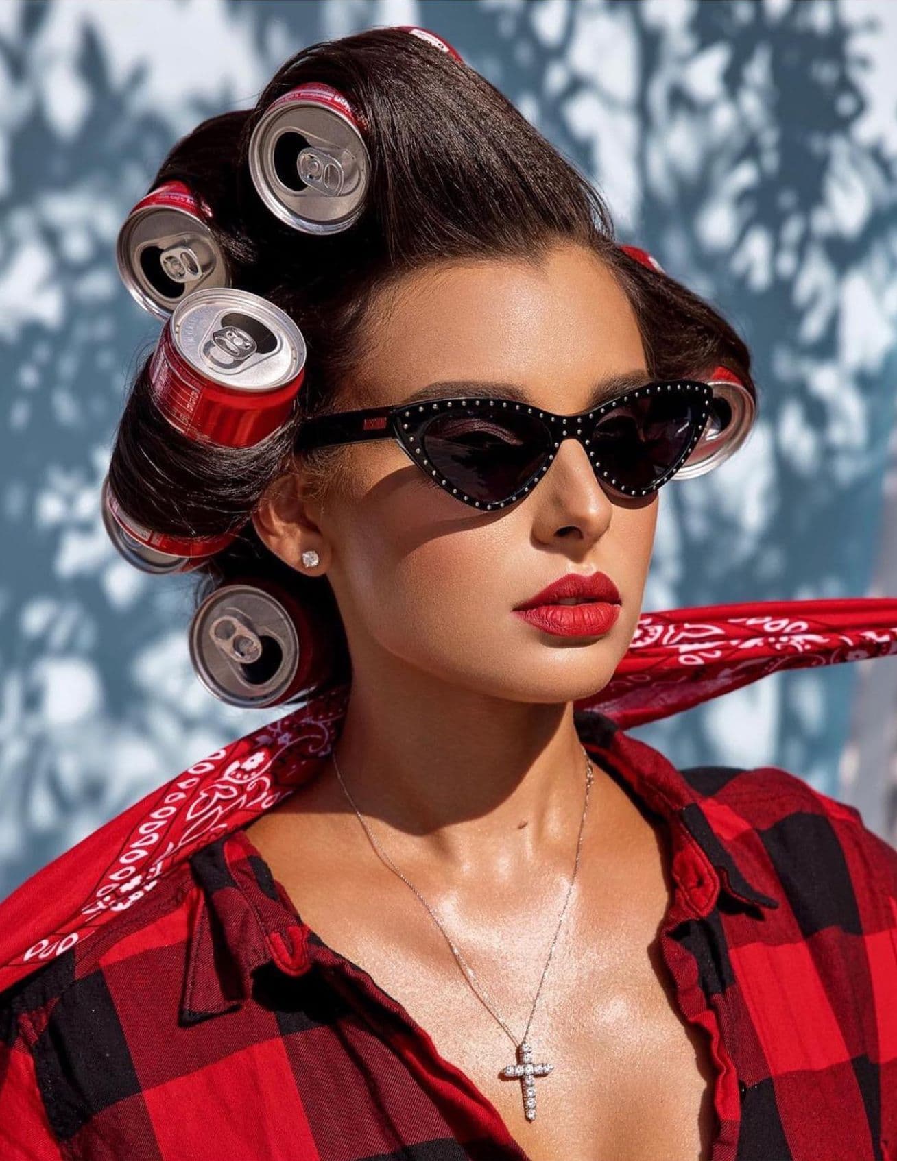 A stylish woman models hair with red soda can curlers, red lipstick, and a red flannel shirt in a commercial photo.
