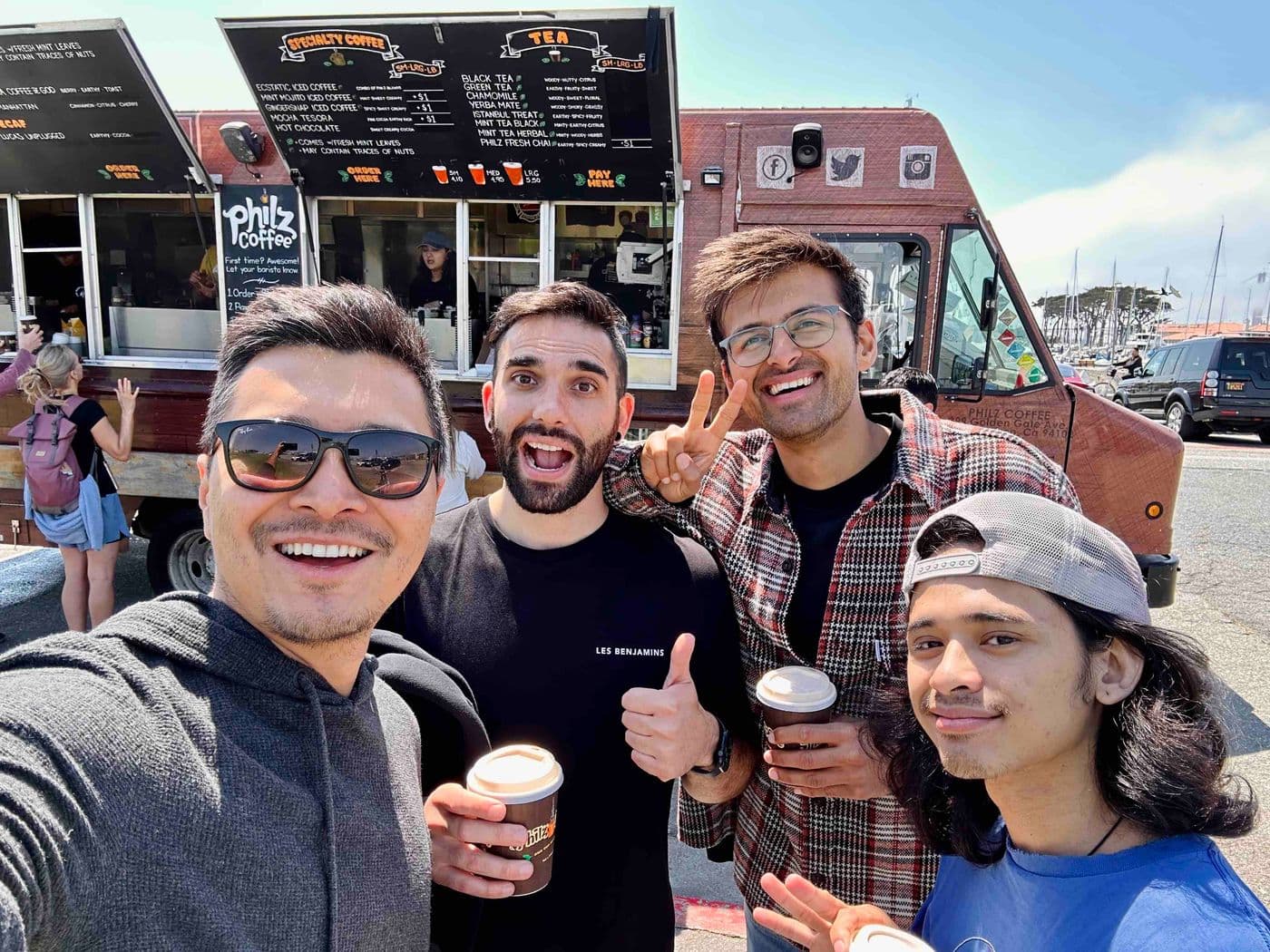 Four friends smile with Philz Coffee in front of a Philz Coffee truck.