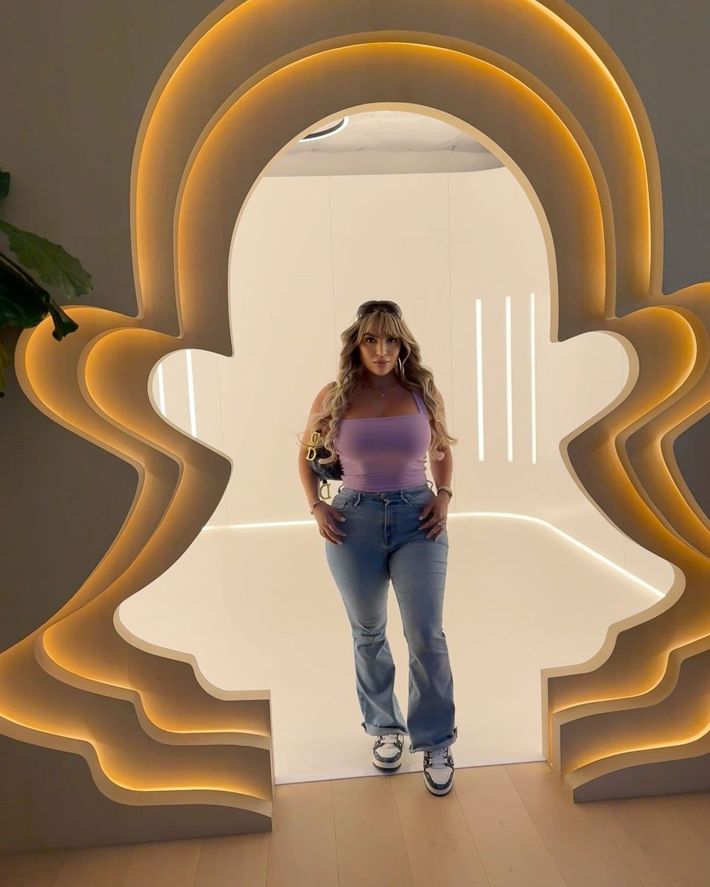 Model Ara Bozorgian poses in a lavender top and jeans in front of an illuminated Snapchat ghost logo archway.