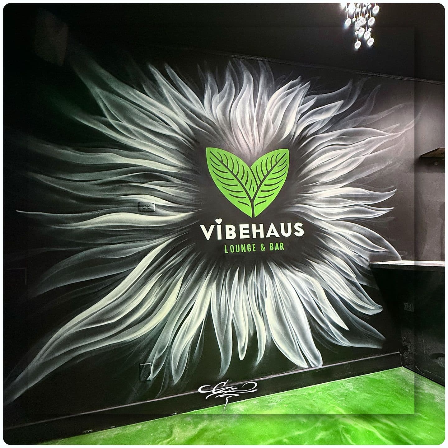 A custom wall mural for Vibehaus Lounge & Bar, featuring their green leaf logo inside a white, flowing sunburst design.