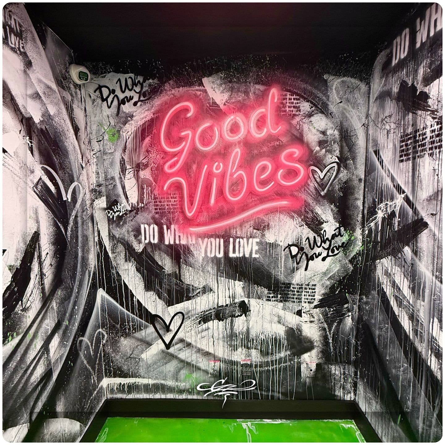 A custom mural featuring a pink neon 'Good Vibes' sign against a black-and-white abstract, graffiti-style background.