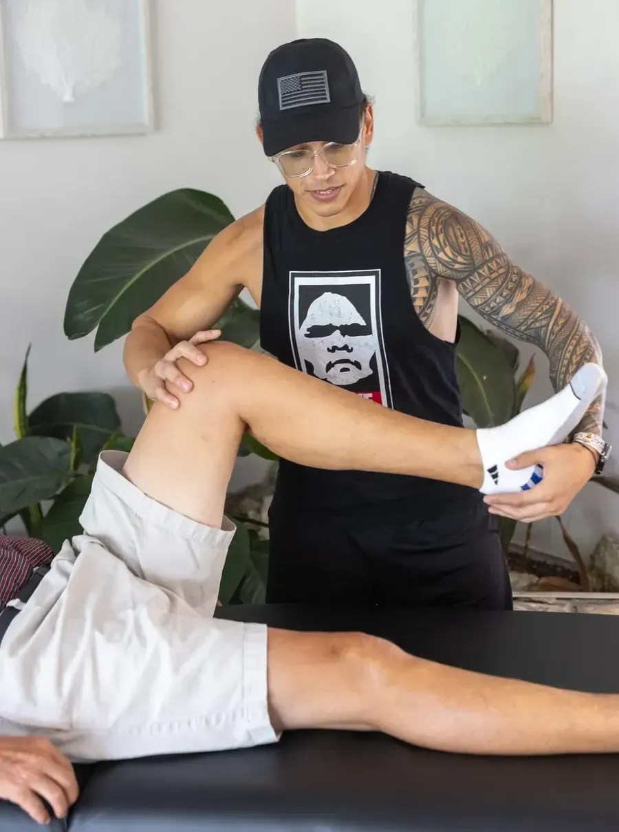 A stretch therapist with tattoos assisting a person with leg stretches on a table.