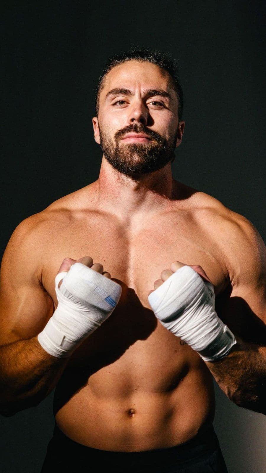 Professional boxer Tristan Hamm posing shirtless with his fists wrapped in white athletic tape.