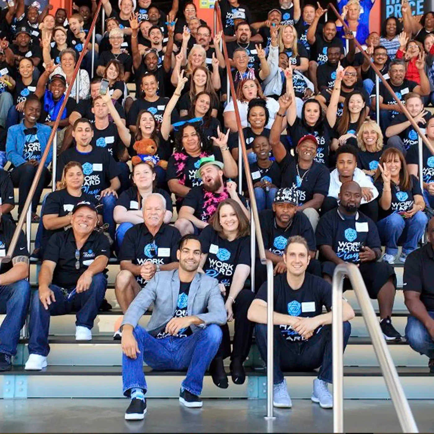 Large group of people wearing matching 'Work Hard Play Hard' t-shirts posing on steps; David Runyon is in the front row.