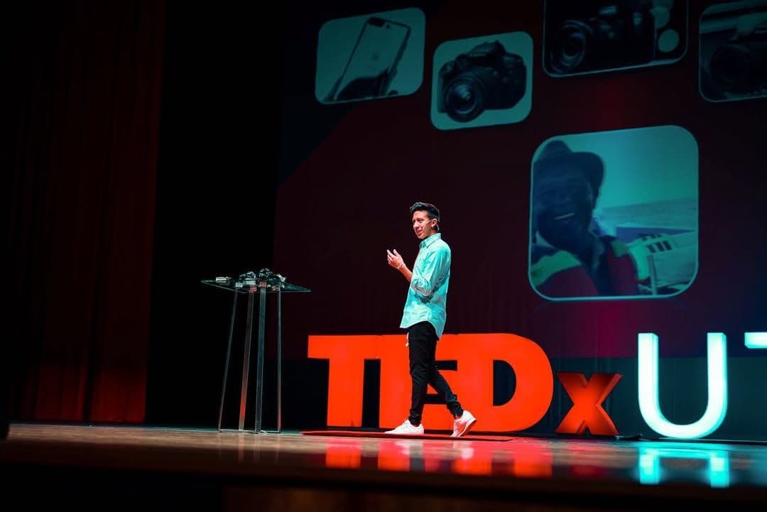 Erick on a TEDx stage, presenting with slides of camera equipment in the background.