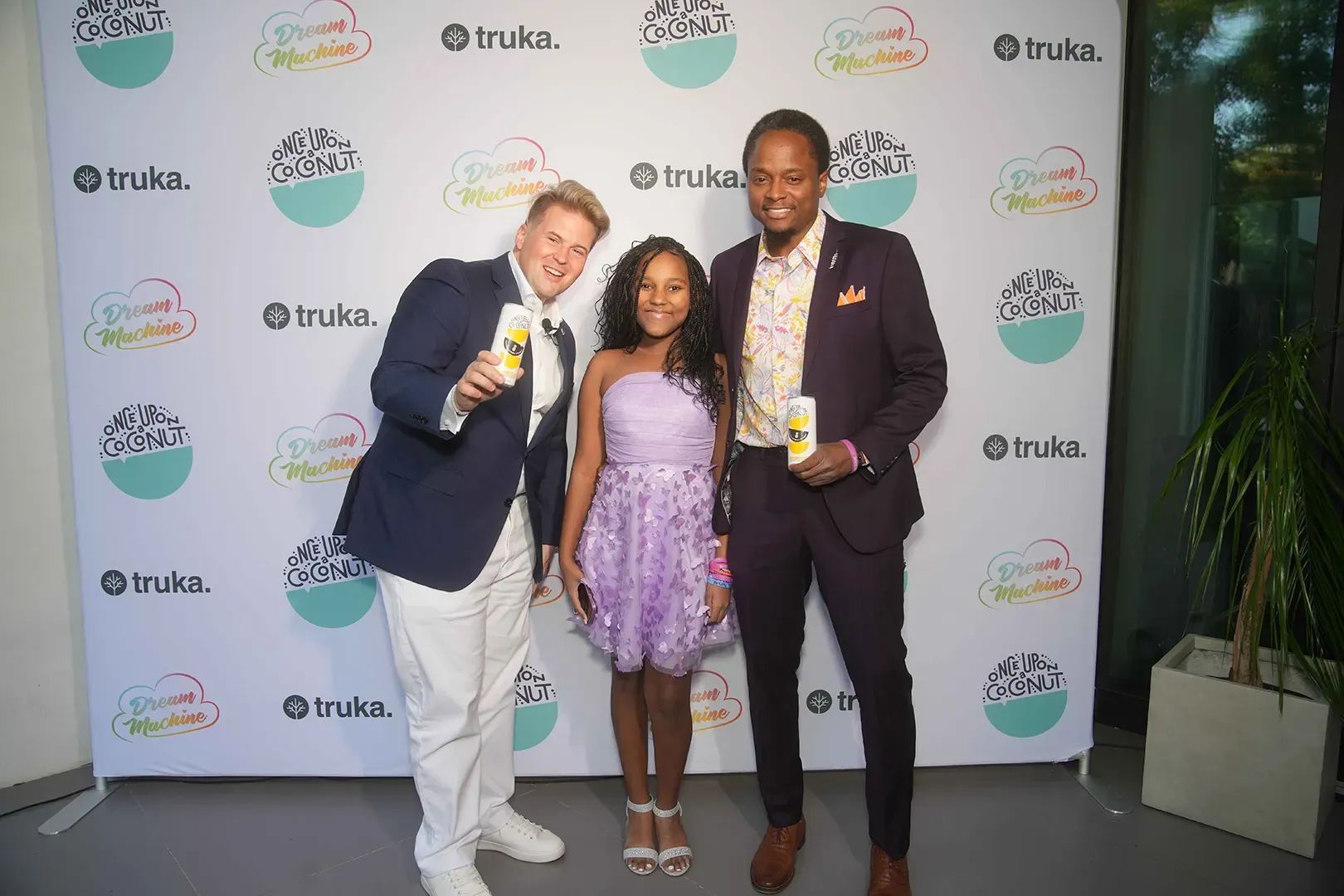 Charlie Rocket stands with two people posing in front of a branded backdrop, each holding a can of Once Upon a Coconut.
