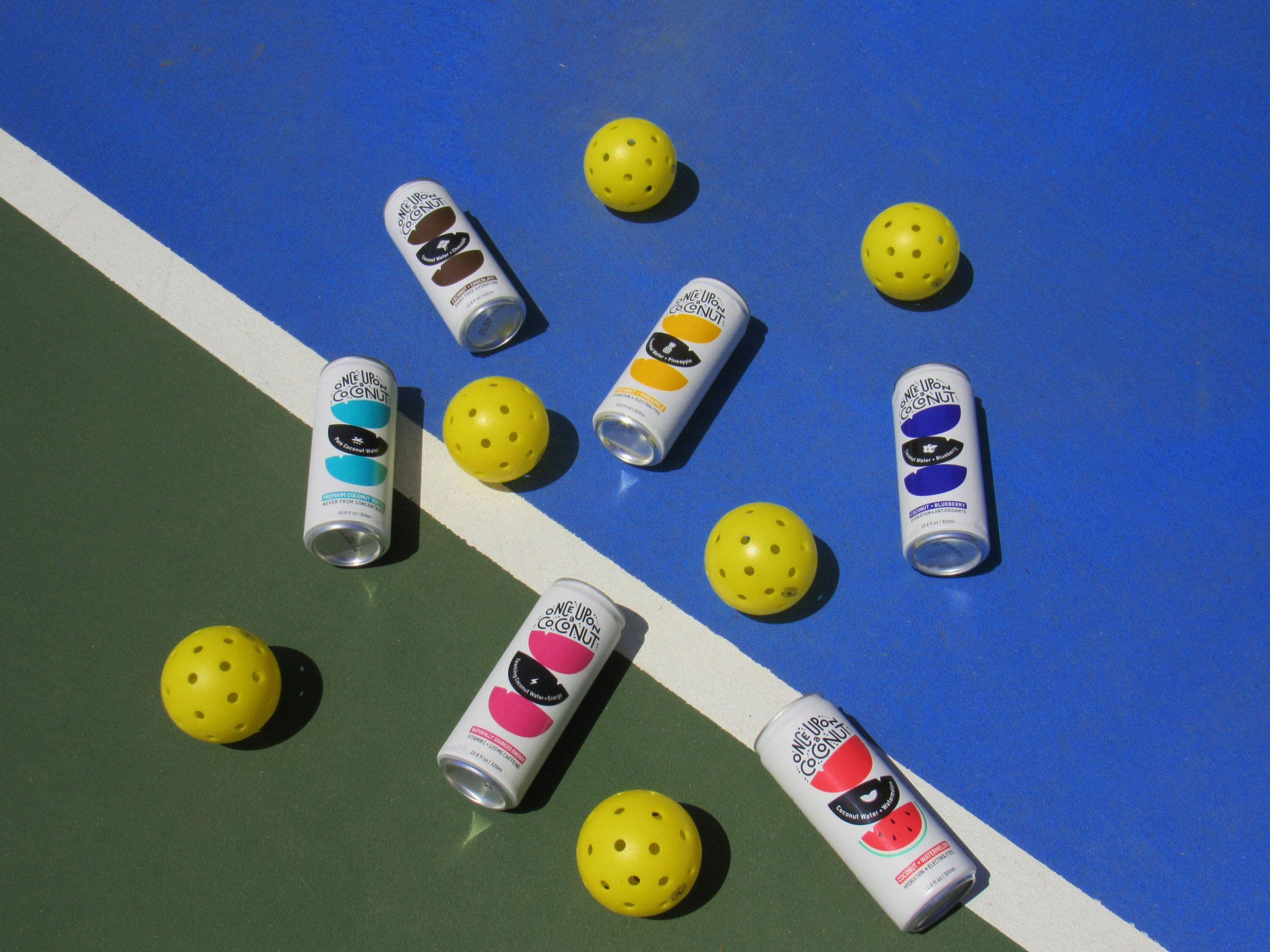 Pickleballs and variety of coconut drinks scattered on blue and green pickleball court.
