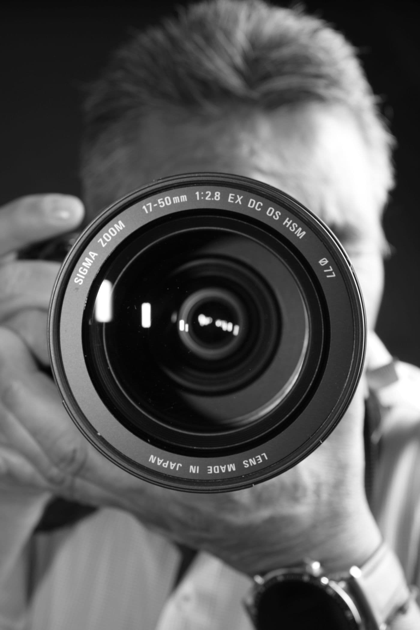 Black and white close-up of a photographer holding a camera lens, captured in a vertical shot.