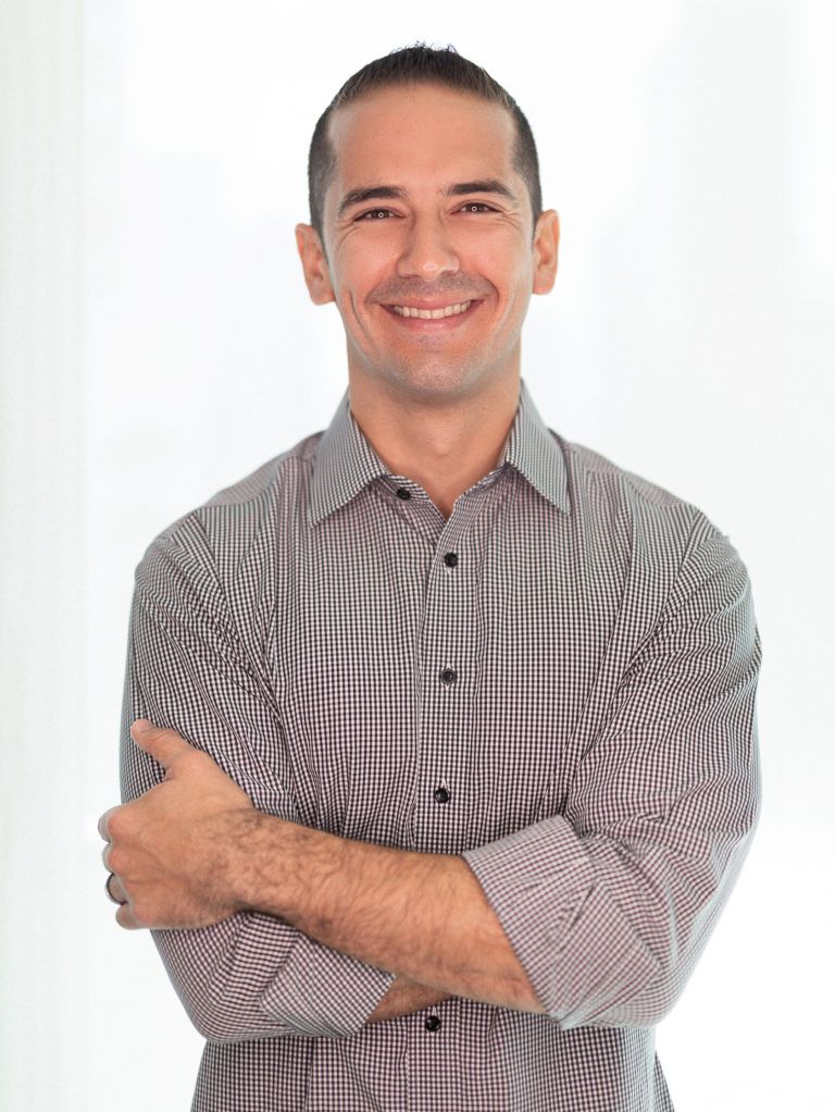 Smiling headshot of Alex Arguelles in a checkered shirt with arms crossed.