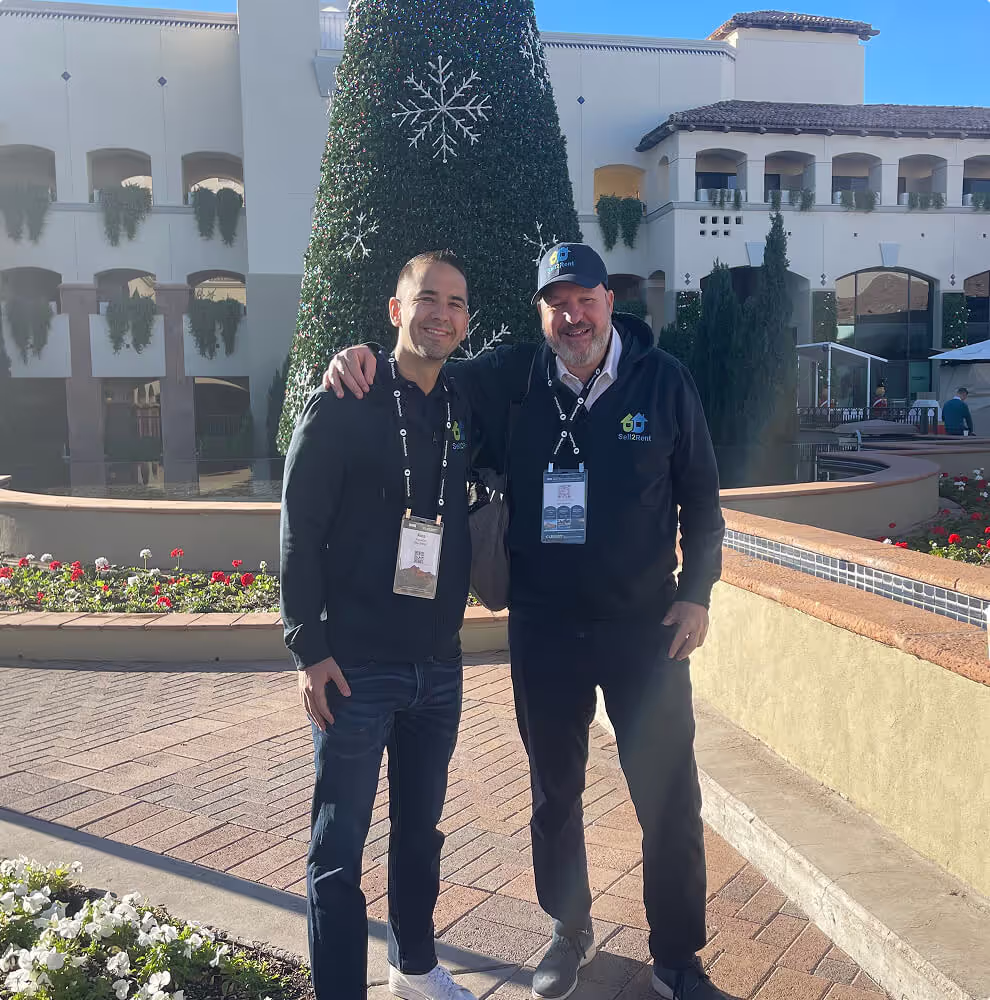Alex Arguelles and Daniel Kattan pose near a large outdoor Christmas tree and fountain.