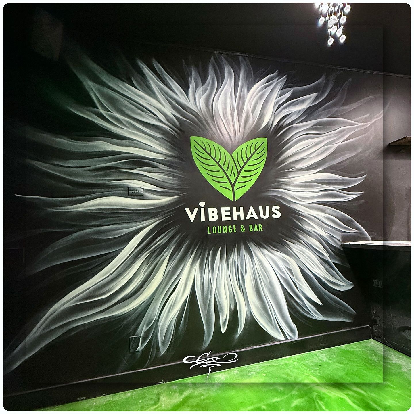 A custom wall mural for Vibehaus Lounge & Bar, featuring their green leaf logo inside a white, flowing sunburst design.