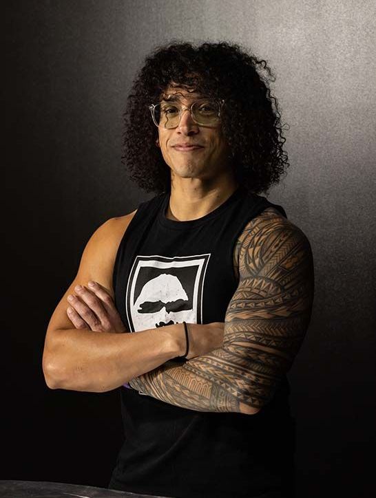 Portrait of mobility specialist Joel, arms crossed, sporting arm tattoo and glasses.