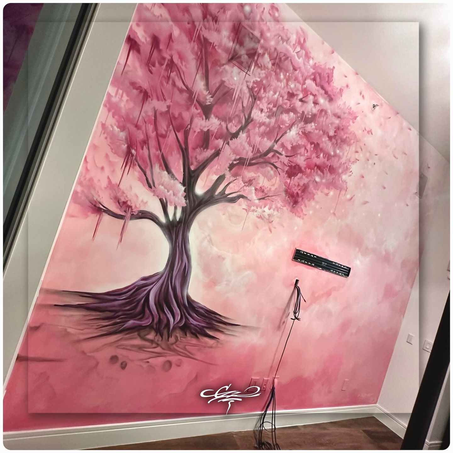 A large, custom children's wall mural of a stylized pink cherry blossom tree painted on an angled wall in a home.