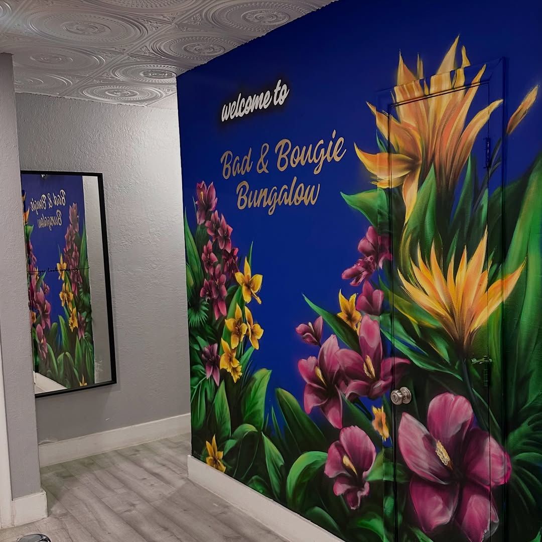 Custom residential mural on a blue wall featuring tropical flowers and the text 'welcome to Bad & Bougie Bungalow'.