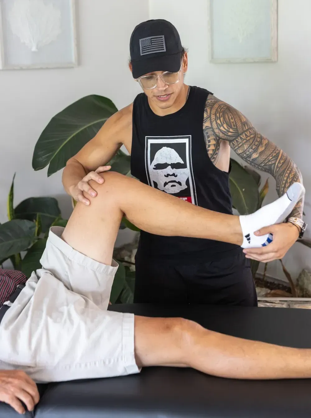 A stretch therapist with tattoos assisting a person with leg stretches on a table.