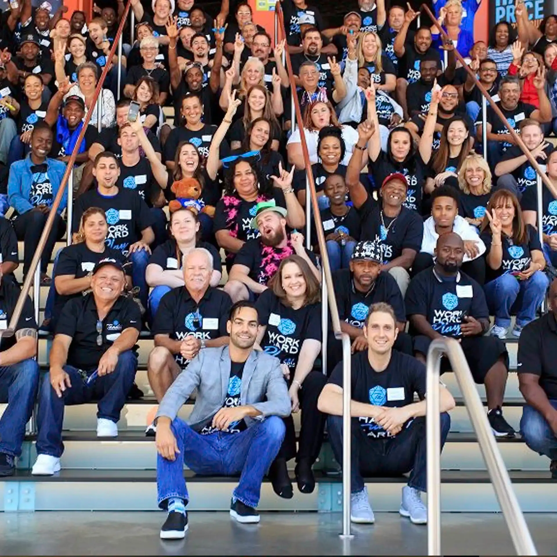 Large group of people wearing matching 'Work Hard Play Hard' t-shirts posing on steps; David Runyon is in the front row.